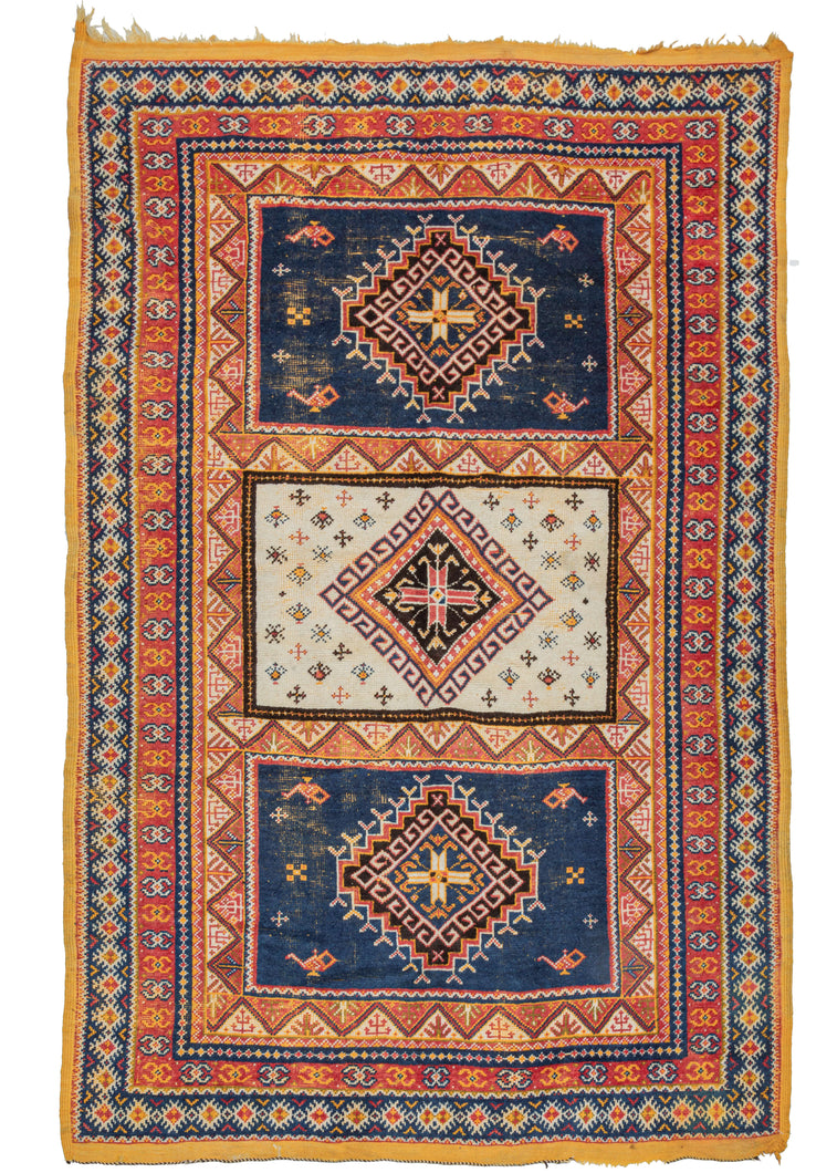 Mid century Moroccan Taznakht area rug featuring a field of three compartments each with a central latch-hooked diamond motif. The center compartment is bright ivory and filled with small protection symbols. The top and bottom compartments feature a more sparse design around a stepped diamond on a navy ground. Of note in the top and bottom compartments are the depiction of oil or 