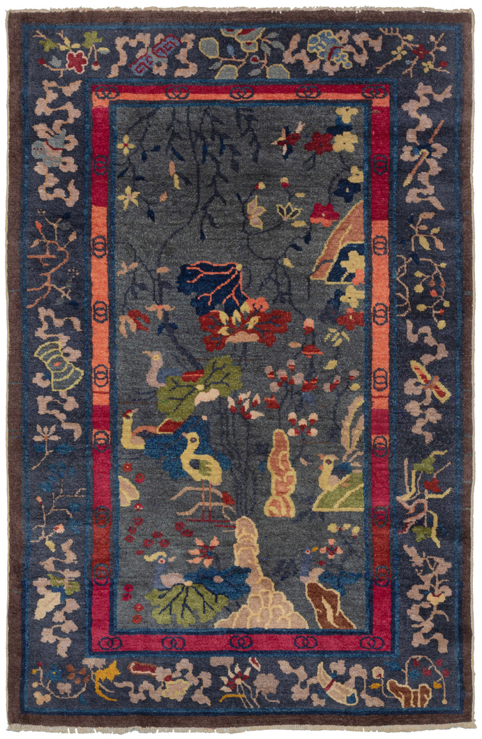 Chinese small deco rug featuring a water scene of various scholar stones, birds, and vegetation. The varied blues, greens, oranges, reds, and yellow really stand out against a calming periwinkle ground. Framed by an energetic inner border of varied blocks of red, oranges, and pink and well-spaced interlocking circles, the main border features the eight auspicious symbols of Buddhism on a darker shade of periwinkle.