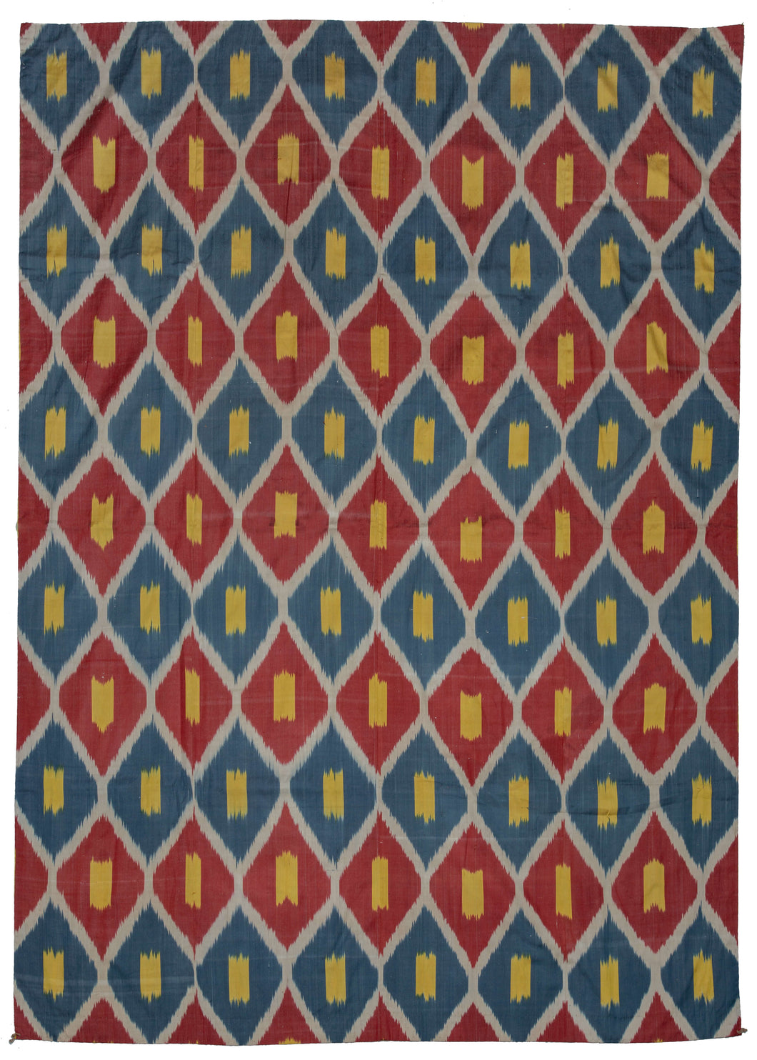 Silk Uzbek handwoven ikat textile featuring a repeating interlocking diamond motif in blue, red, and yellow with a white outline. The back is a brightly colored paisley print on synthetic fabric. 