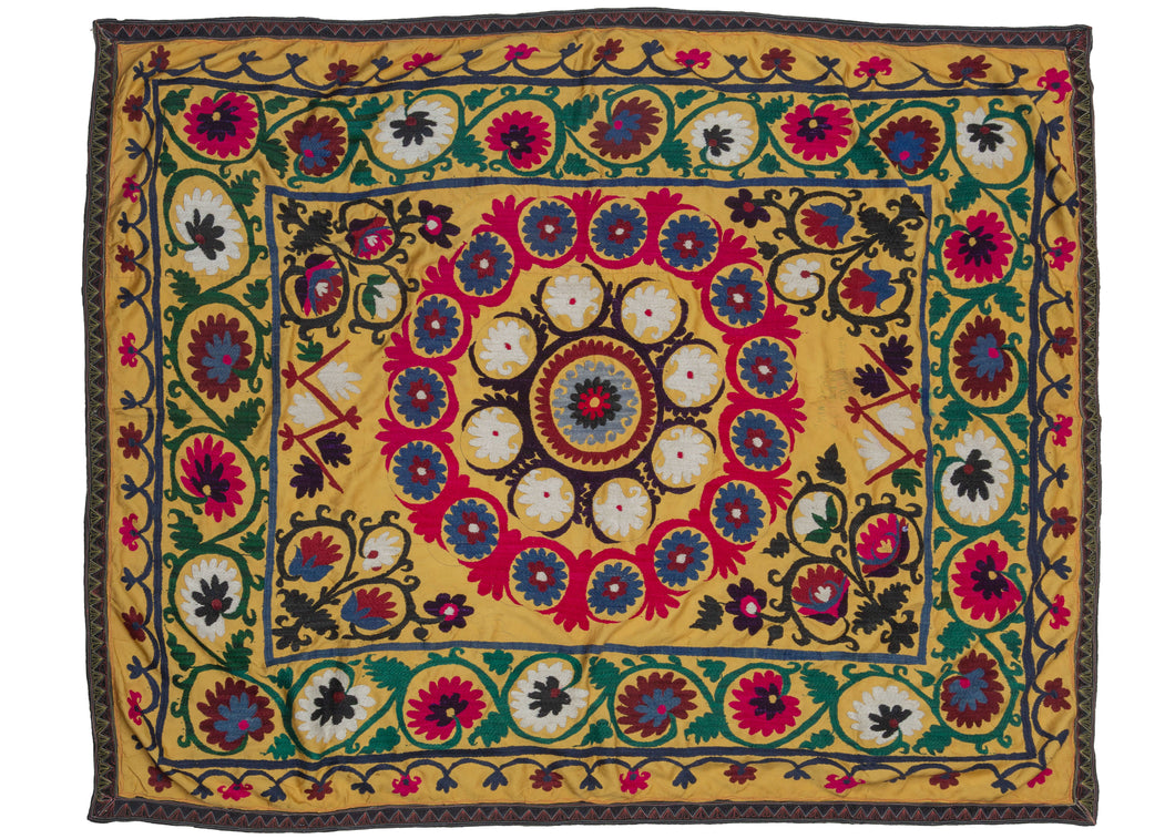 This Vintage Uzbek Suzani features a central mandala with a multilayered arrangement of flowers in blue, white, and bright pink framed by a large outer border of scrolling green vines with flowers in burgundy, pink and white. With little to no space of this textile untouched, the majority of this piece has been meticulously embroidered. 